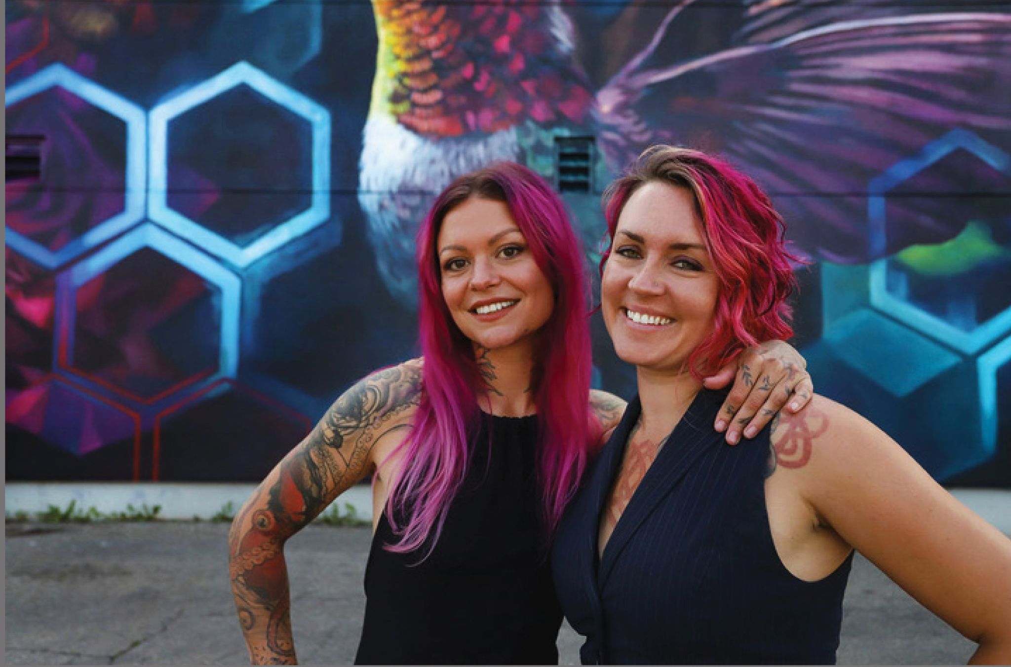 LALA Art LALA Art (Lacey Jane Wilburn & Layla Folkmann) stand in front of a coulourful mural they have created.