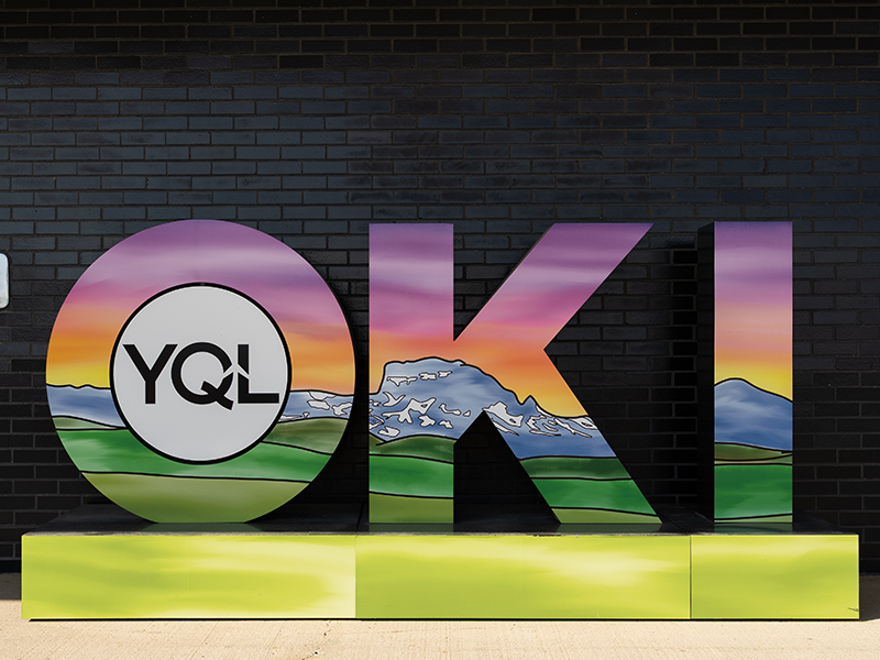 OKI by Mariah (Omah’kaistaawakaakii) Gladstone OKI sculpture at the Lethbridge airport by Mariah (Omah’kaistaawakaakii) Gladstone. Across the three letters a vibrant landscape of Chief Mountain with the pinks and oranges of sunset in the sky.