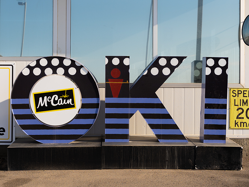 OKI by Serene Weasel Traveller OKI sculpture by Serene Weasel Traveller outside of McCain Foods gate. This design in white, black, red and blue depicts a pictogram man standing on the blue lines of water reflecting on the water treaty.